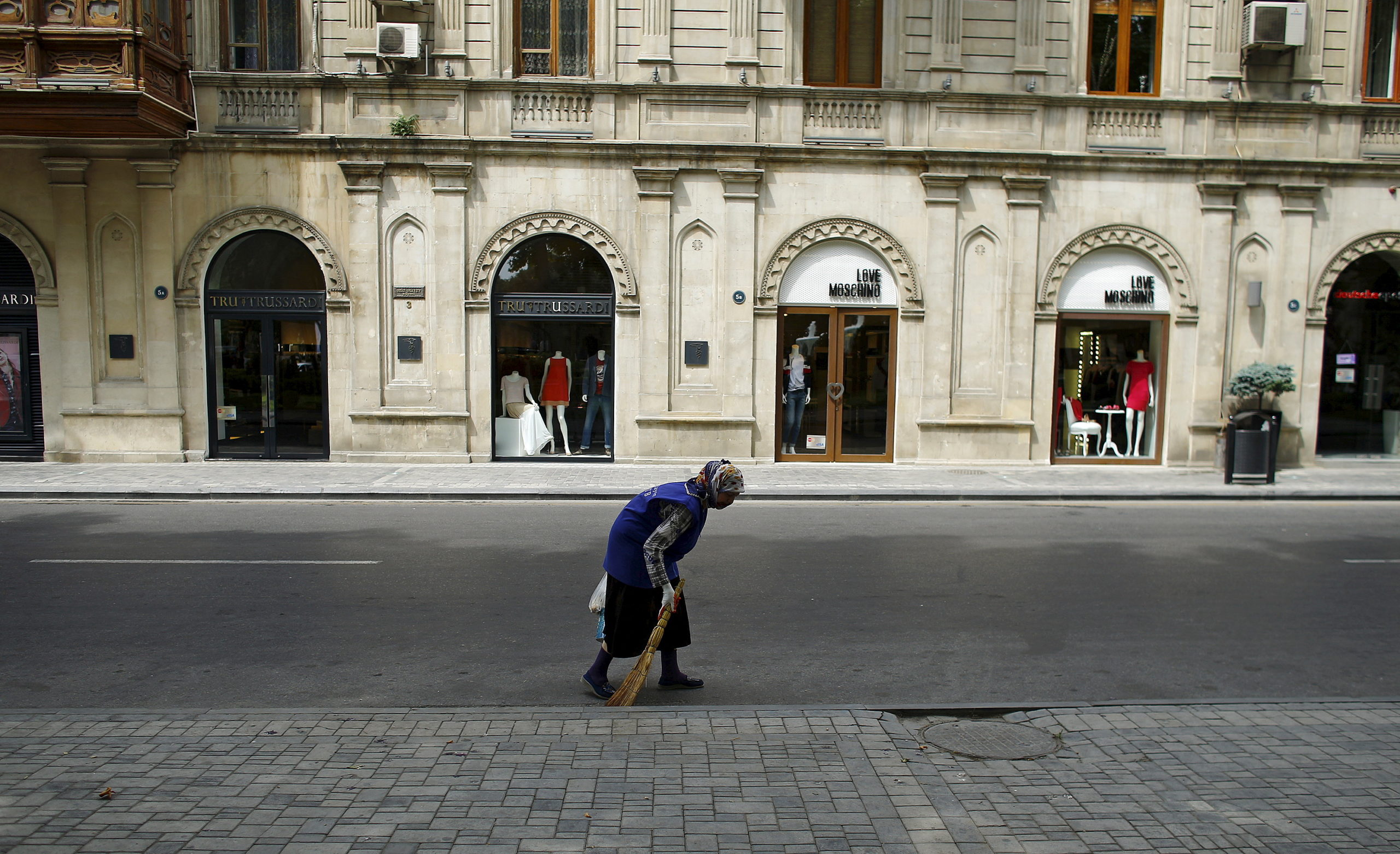 A woman sweeps a street in front of fashion boutiques in Baku, Azerbaijan June 15, 2015. REUTERS/Stoyan Nenov